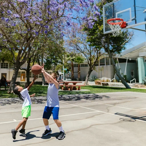 Picture showing two kids playing basketball outsite.
